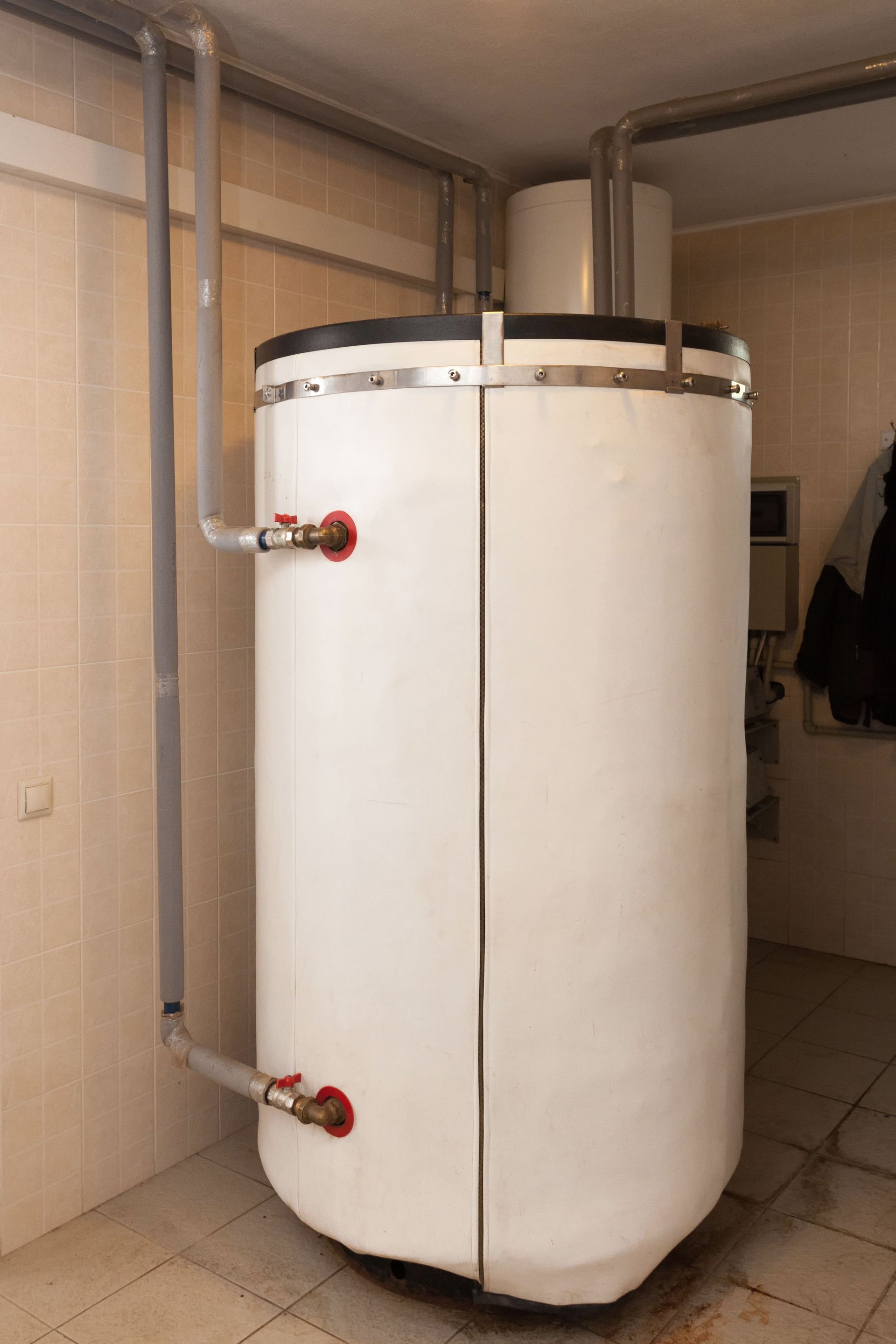 White cylindrical water tank with piping and red valves, indoors.