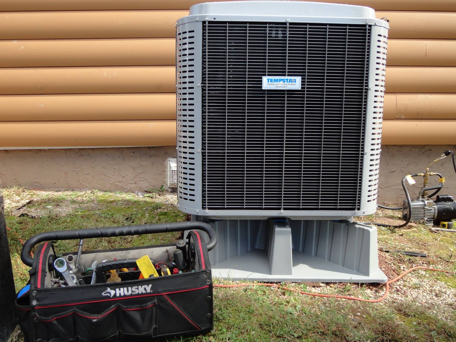 Air conditioning unit next to a toolbox on a concrete base outside a log cabin.