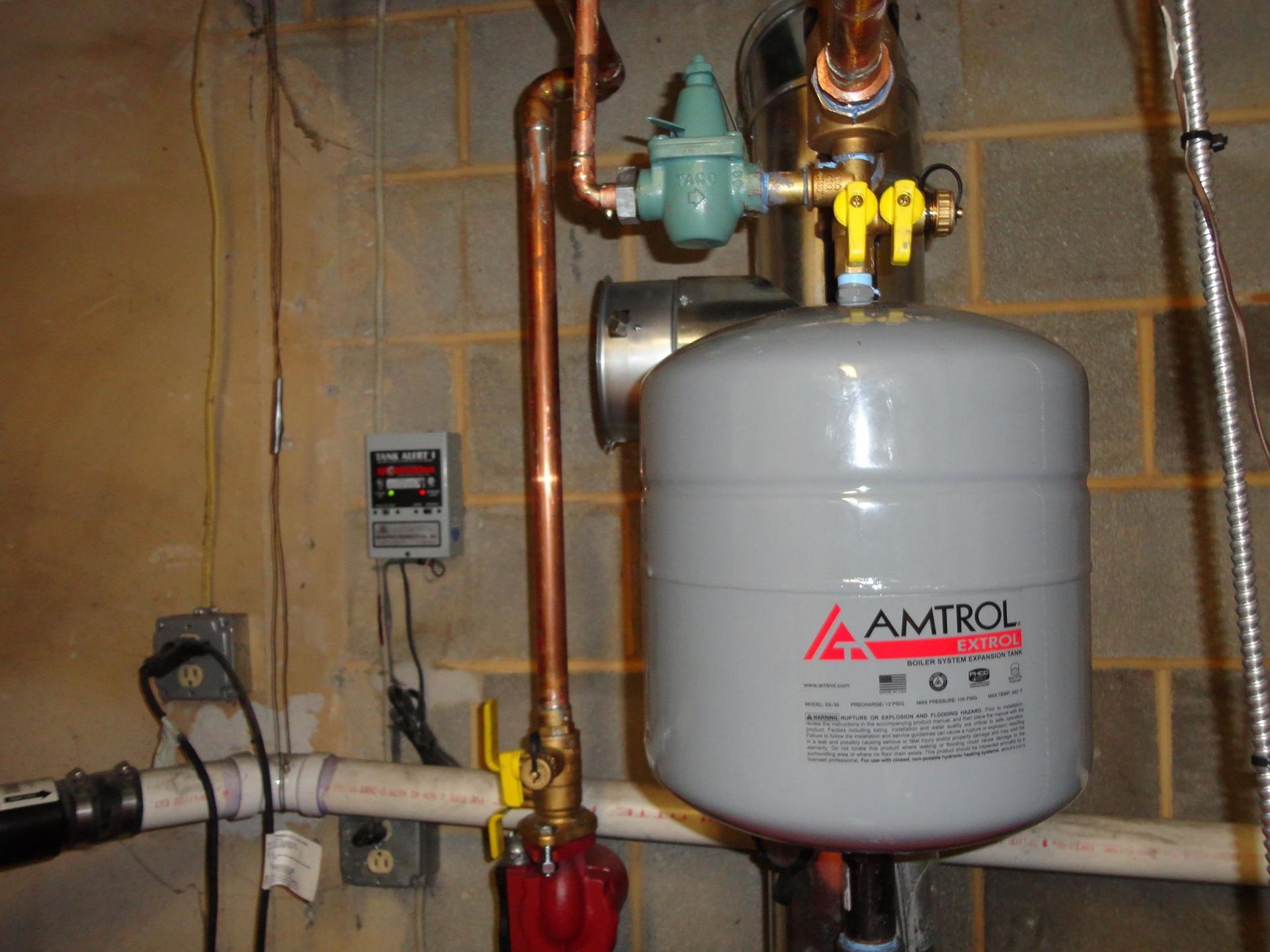 A water pressure system in a basement setting with copper pipes, a gray expansion tank, and a control valve.