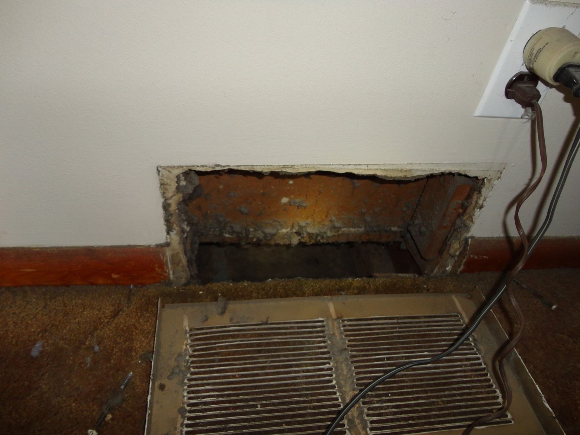 Open air vent in a wall with deteriorated surrounding material and a floor register. Electrical wires are nearby.