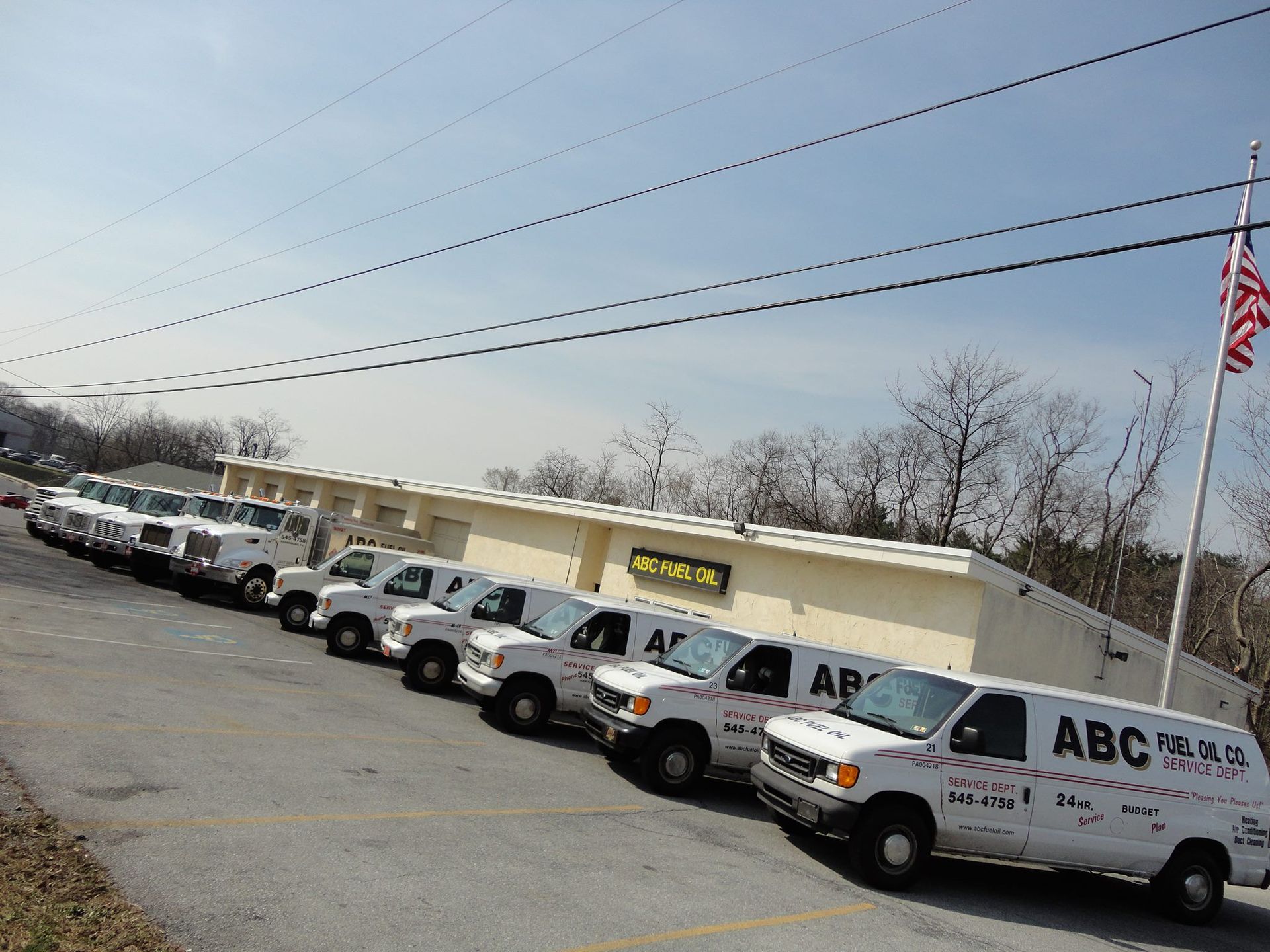 A line of white ABC service vans parked in front of a tan building with an American flag.