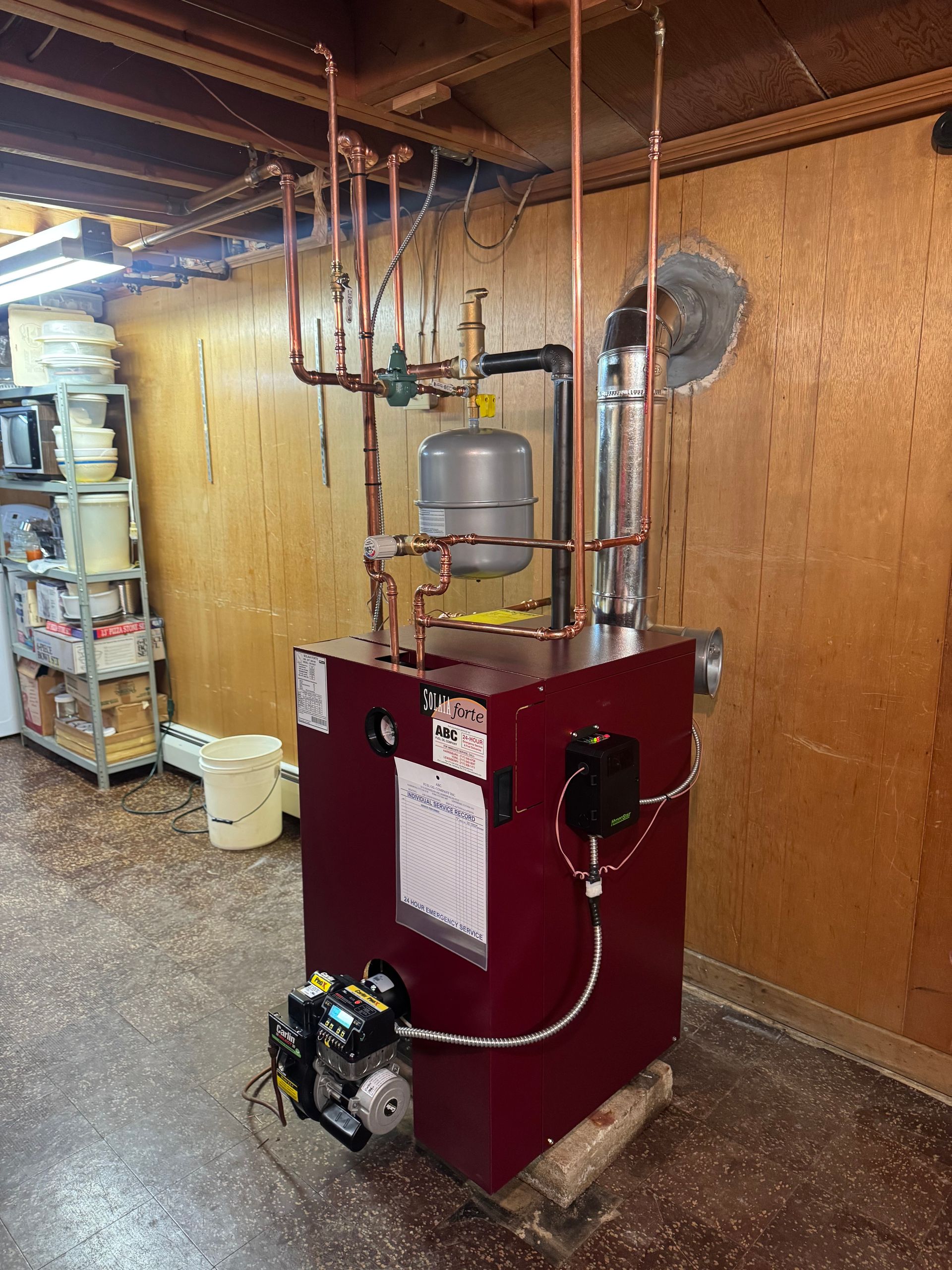 Red heating boiler in a wooden-walled basement with copper pipes and a silver expansion tank.
