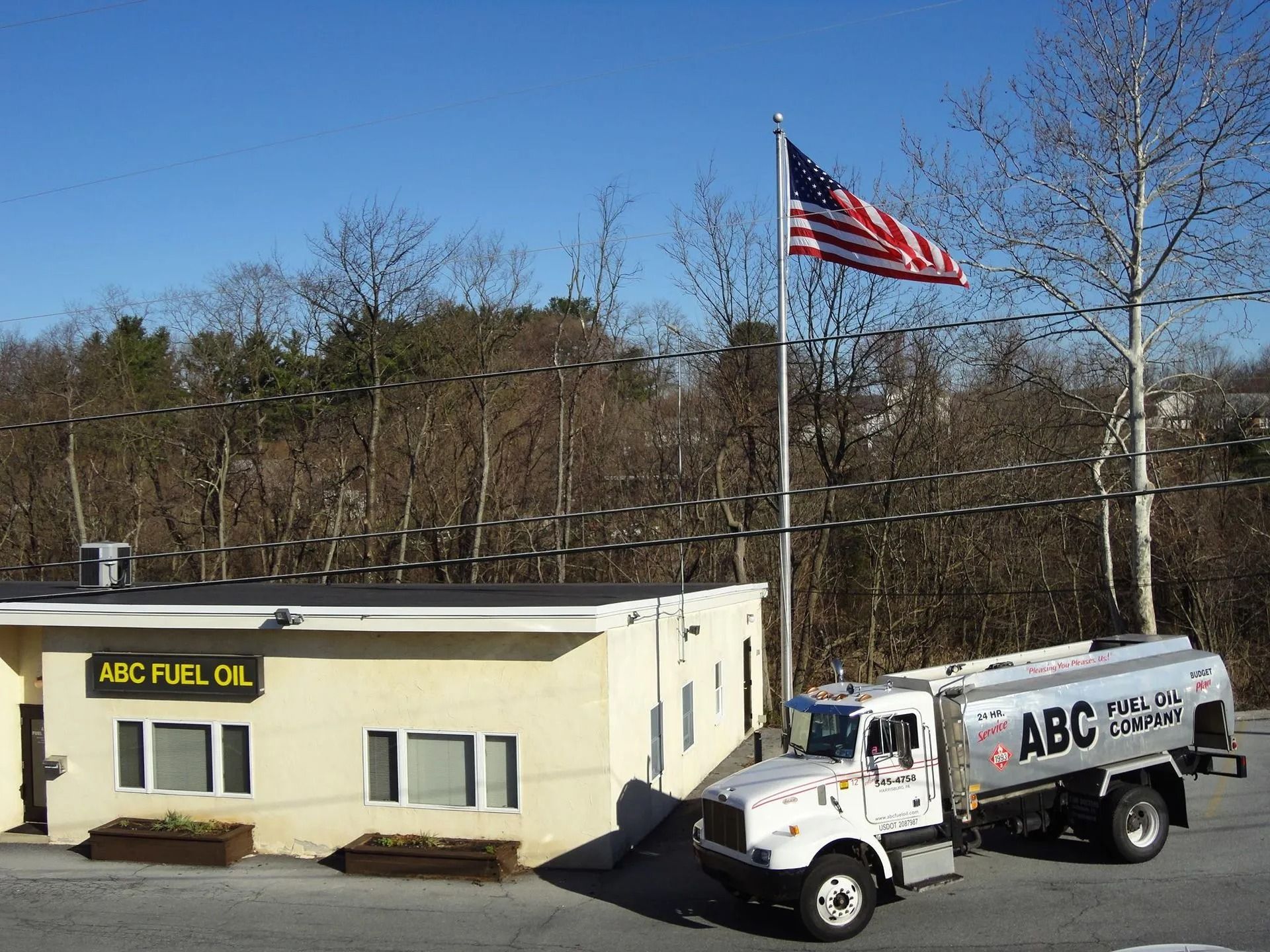 ABC Fuel Oil truck parked outside a small building with an American flag on a sunny day.