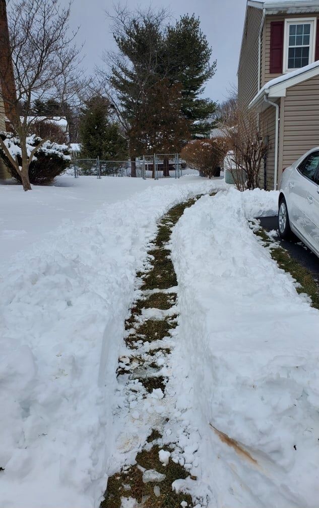 Snow-covered driveway with a path cleared to a house. A car is parked on the right.