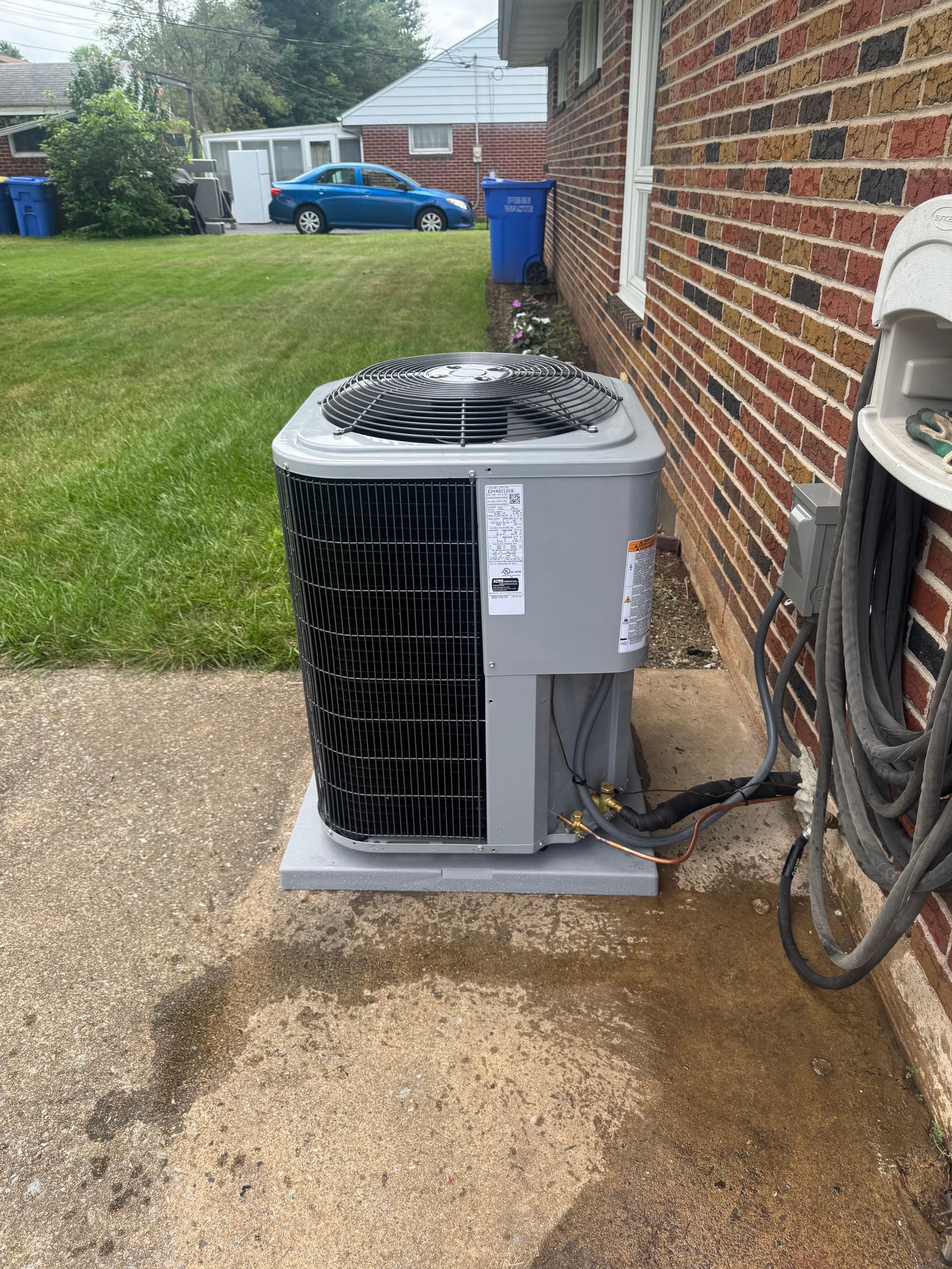 Air conditioning unit on concrete pad next to brick wall and coiled black hose.