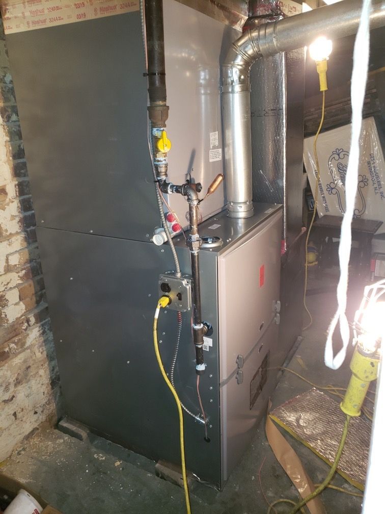 Furnace in a basement; gray metal, gas line visible, two work lights illuminate it.