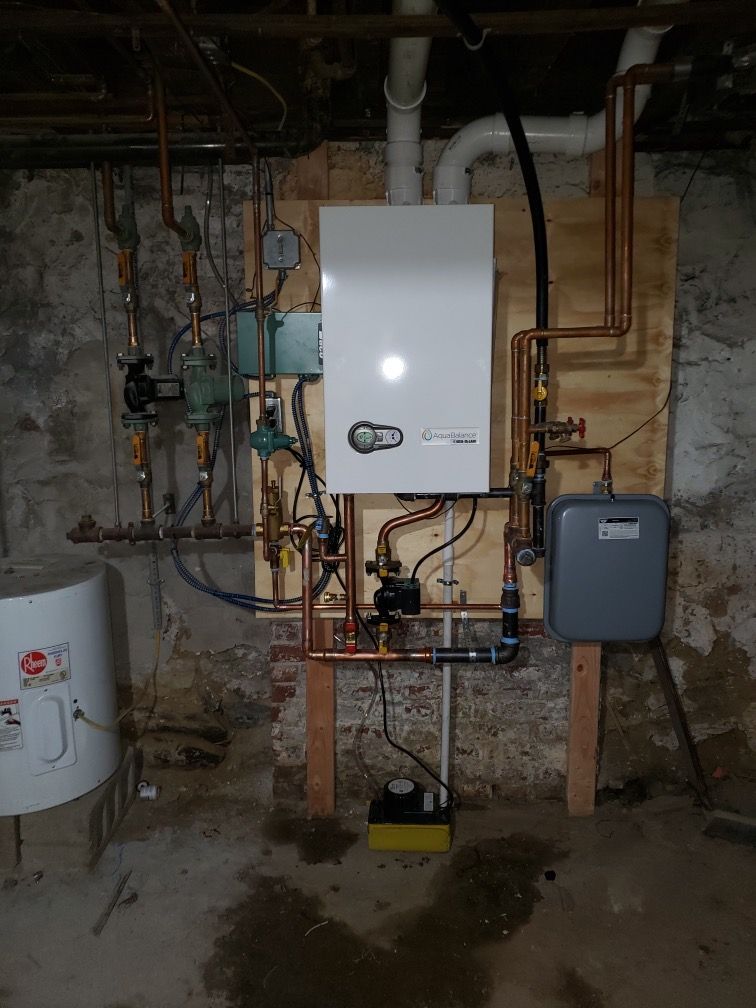 White wall-mounted boiler with copper pipes in a basement setting.