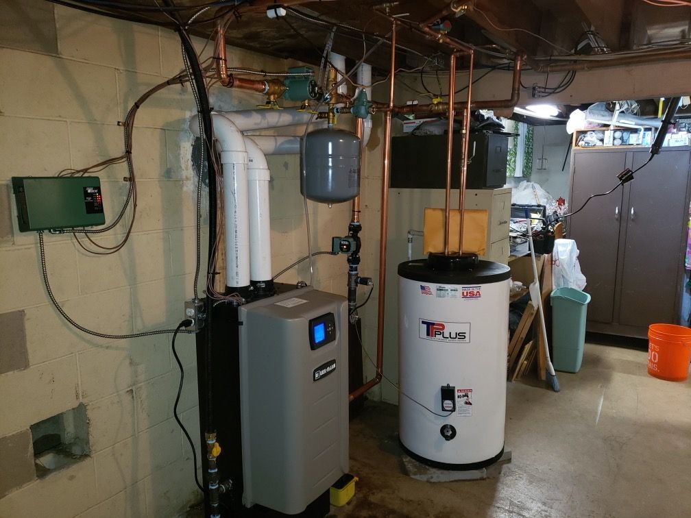 A basement with a gray furnace, white water heater, pipes, and electrical components.