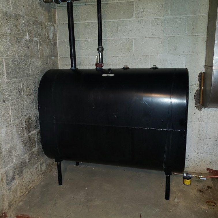 Black oil tank in a basement, with pipes and brick walls.