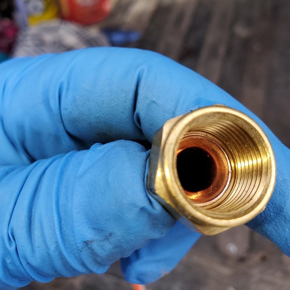 Brass fitting, held in a blue-gloved hand, showing threaded interior.