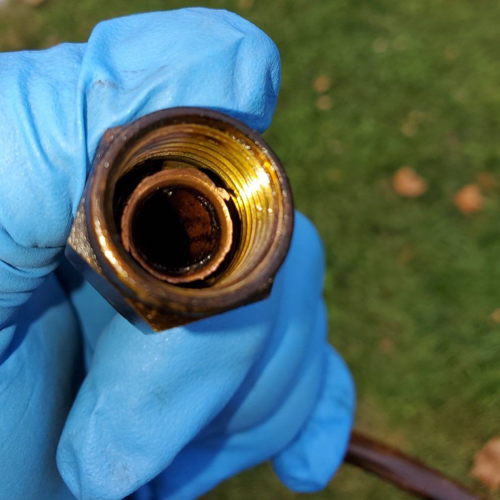 Gloved hand holding a brass fitting with internal threads and a copper tube, outdoors on grass.