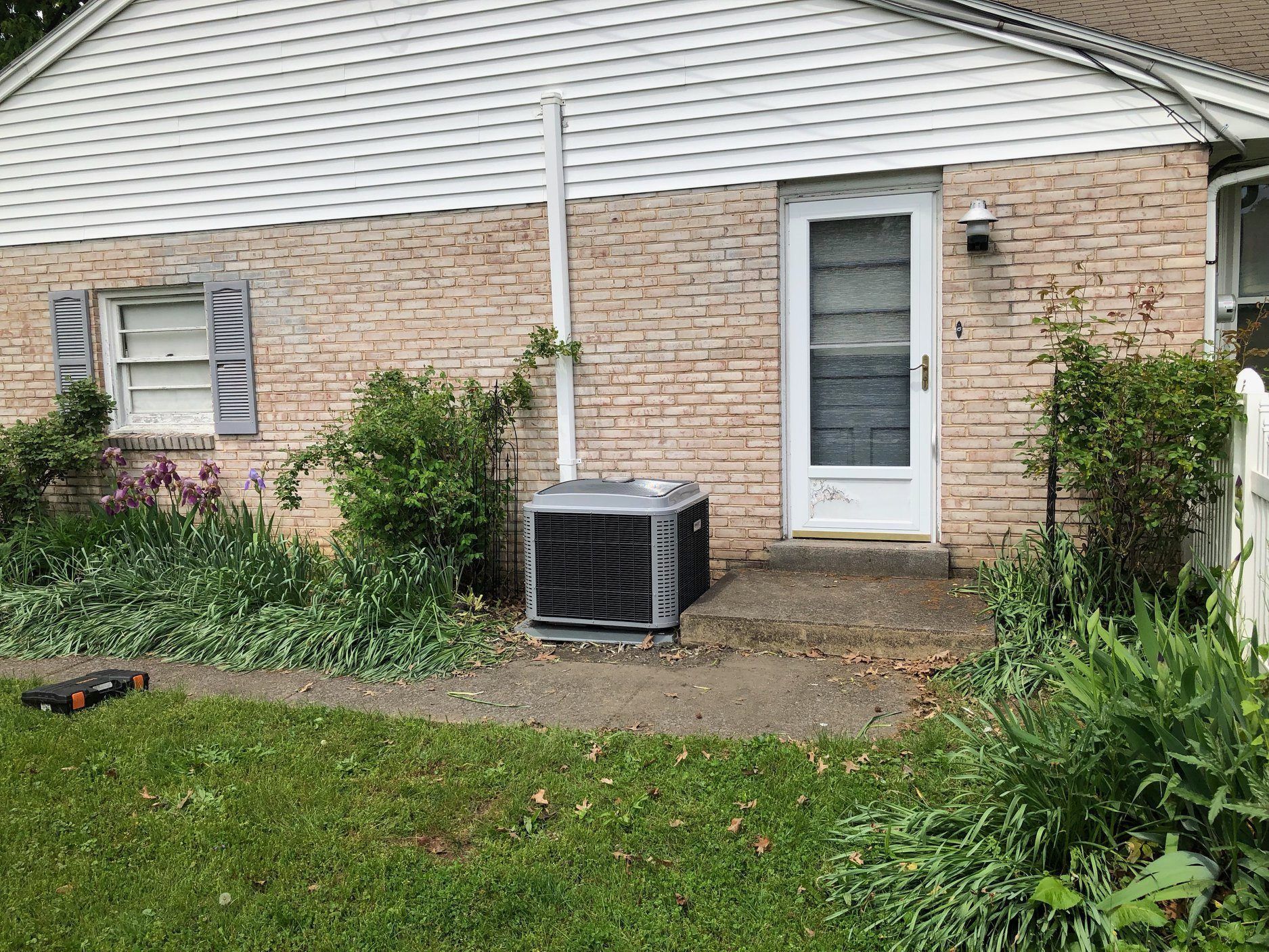 A house with a brick facade and a central AC unit near the back door.