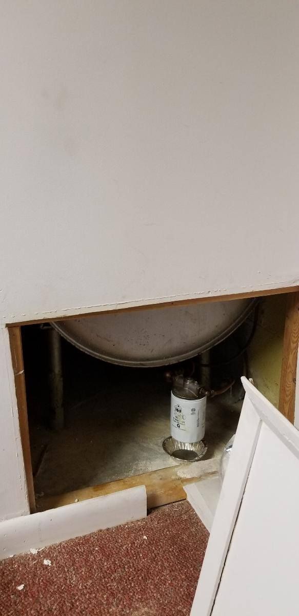 A large, round tank and piping visible through an opening in a wall, carpet on the floor.