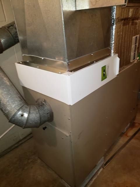 Furnace with metal ductwork, in a basement. White framing around the top.