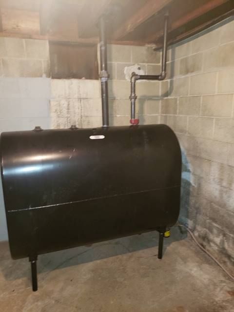 Black oil tank in a basement, with pipes and brick walls visible.
