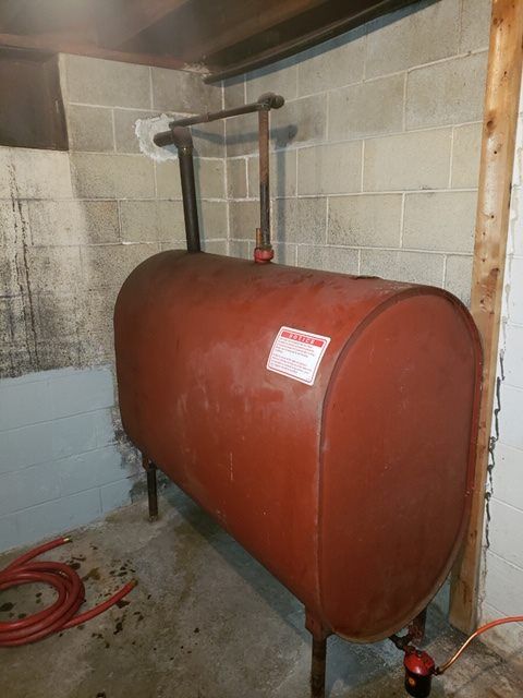 Red oil tank in a basement, with connected pipes and a red hose.