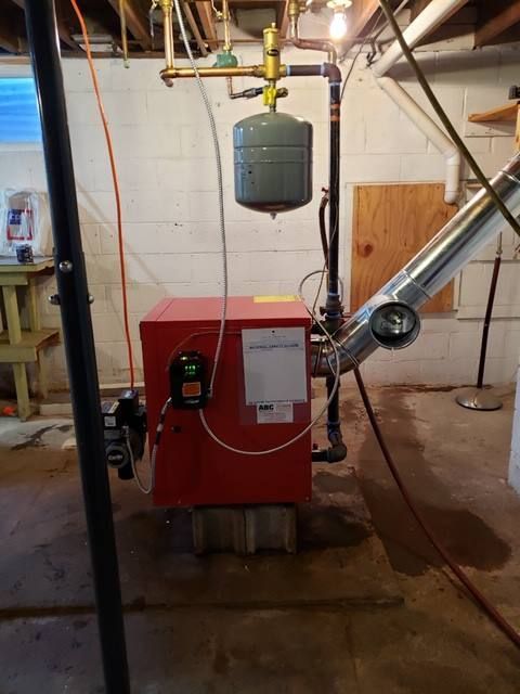 Red oil burner in a basement, with an expansion tank, pipes, and chimney.