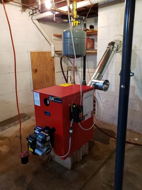 Red oil furnace with silver exhaust pipe in a basement.