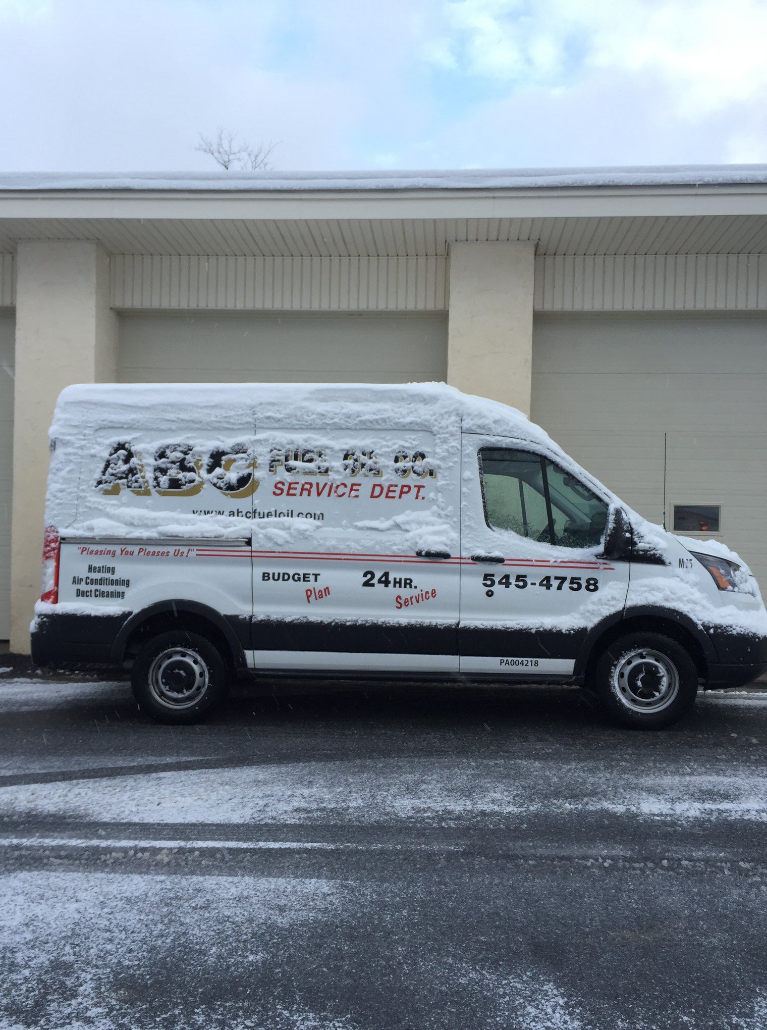 White service van covered in snow parked in front of a building. The van has service information printed on its side.