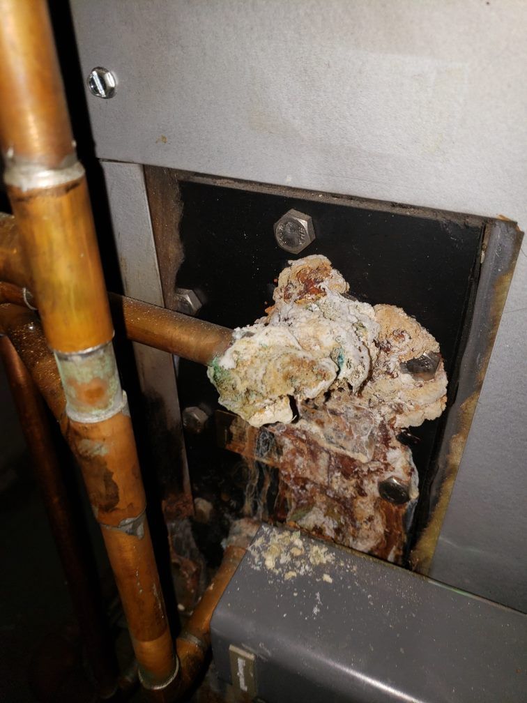 Corroded copper pipes and buildup on a furnace component, next to a metal panel.