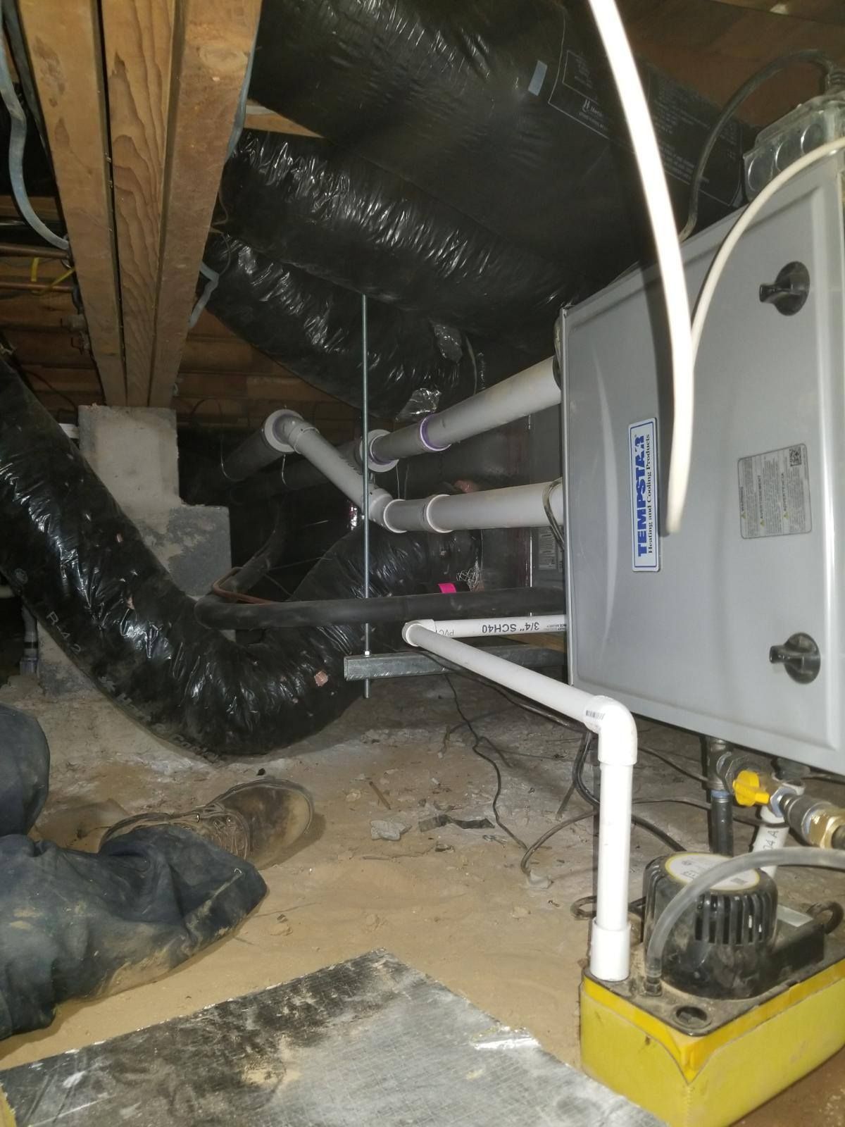 HVAC unit in a crawl space with white PVC pipes, black flexible ductwork, and a condensate pump.