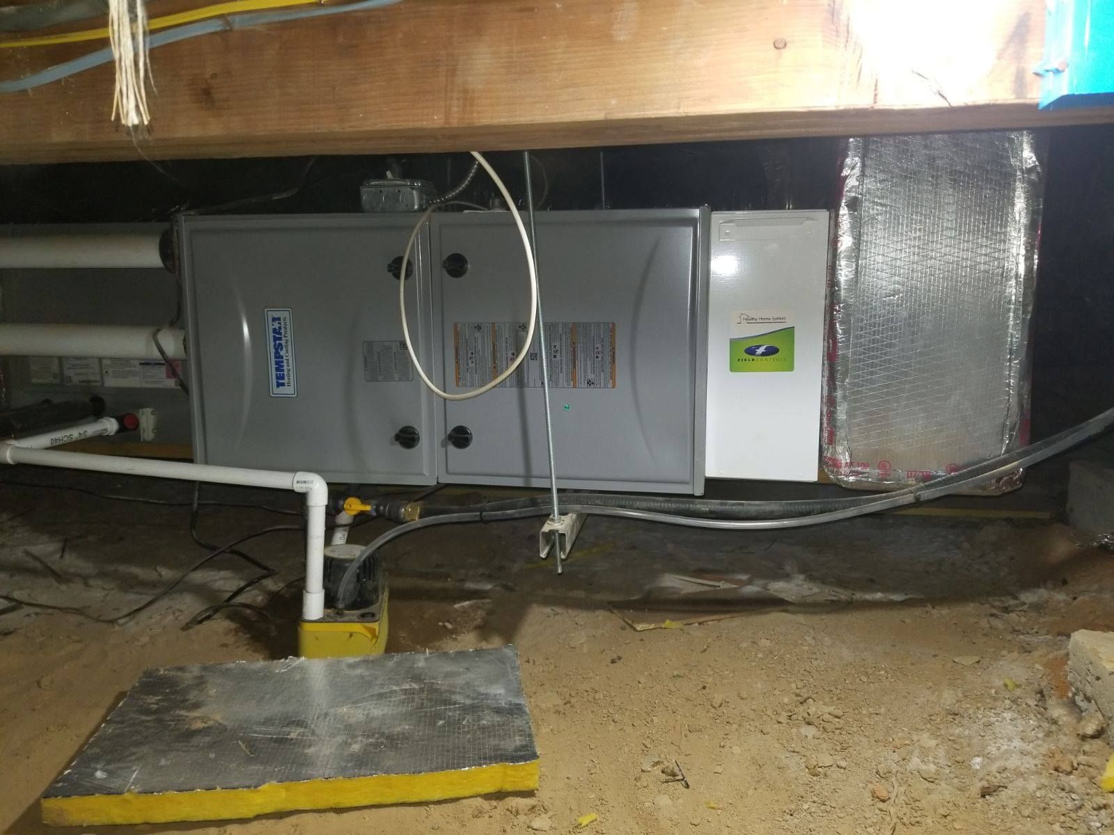 Furnace unit in crawl space with ductwork and plumbing. Gray and white colors.
