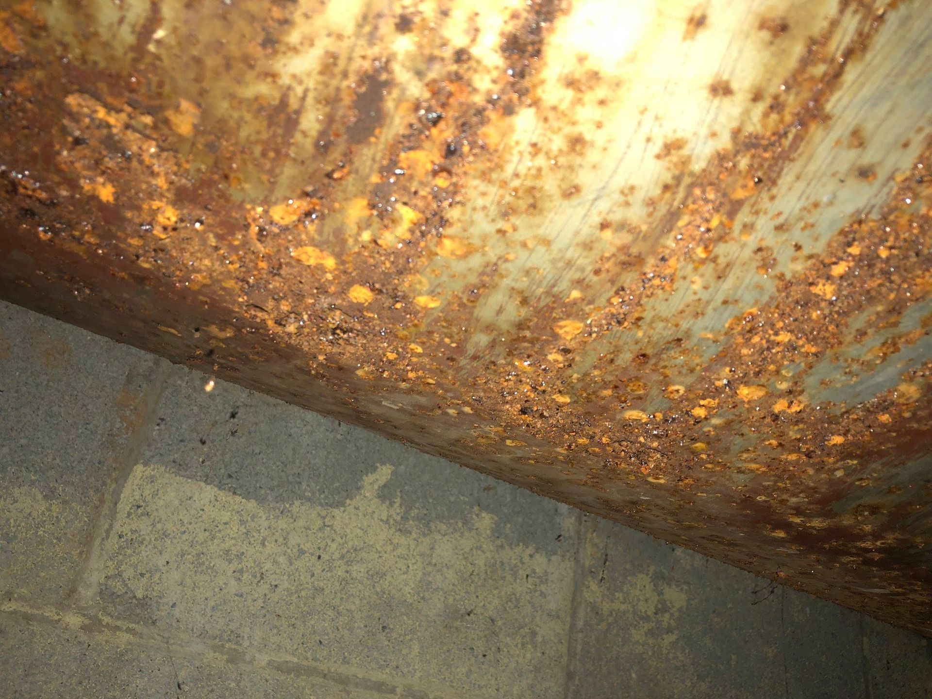 Corroded metal ceiling with rust, above a concrete block wall.
