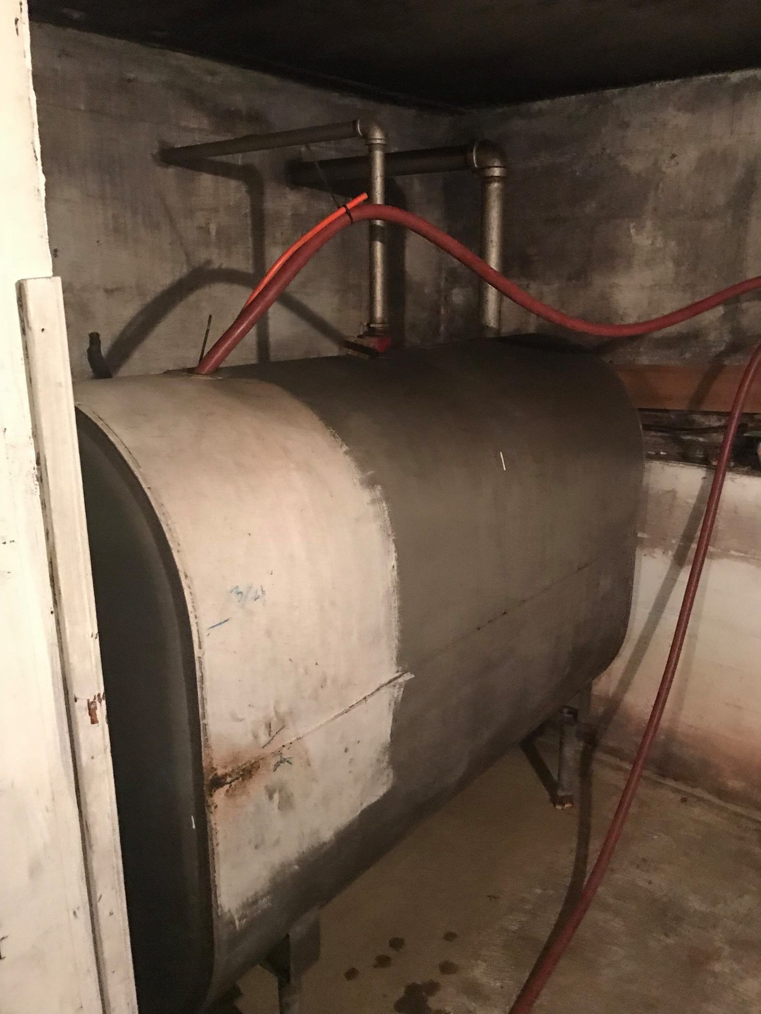 Oil tank in a basement with red fuel lines connected to metal pipes.