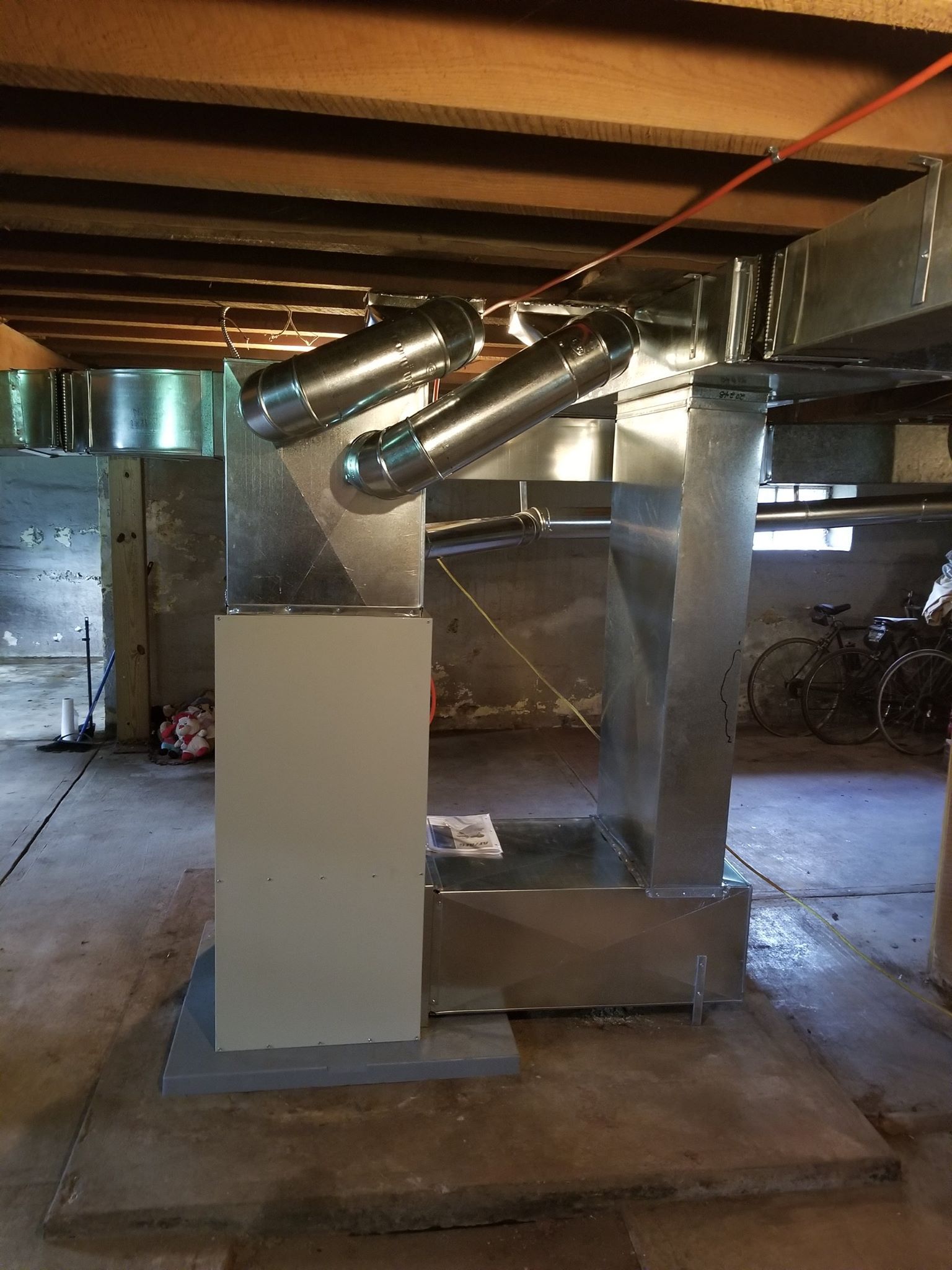 Galvanized ductwork in a basement with silver supports and a light-colored electrical box.