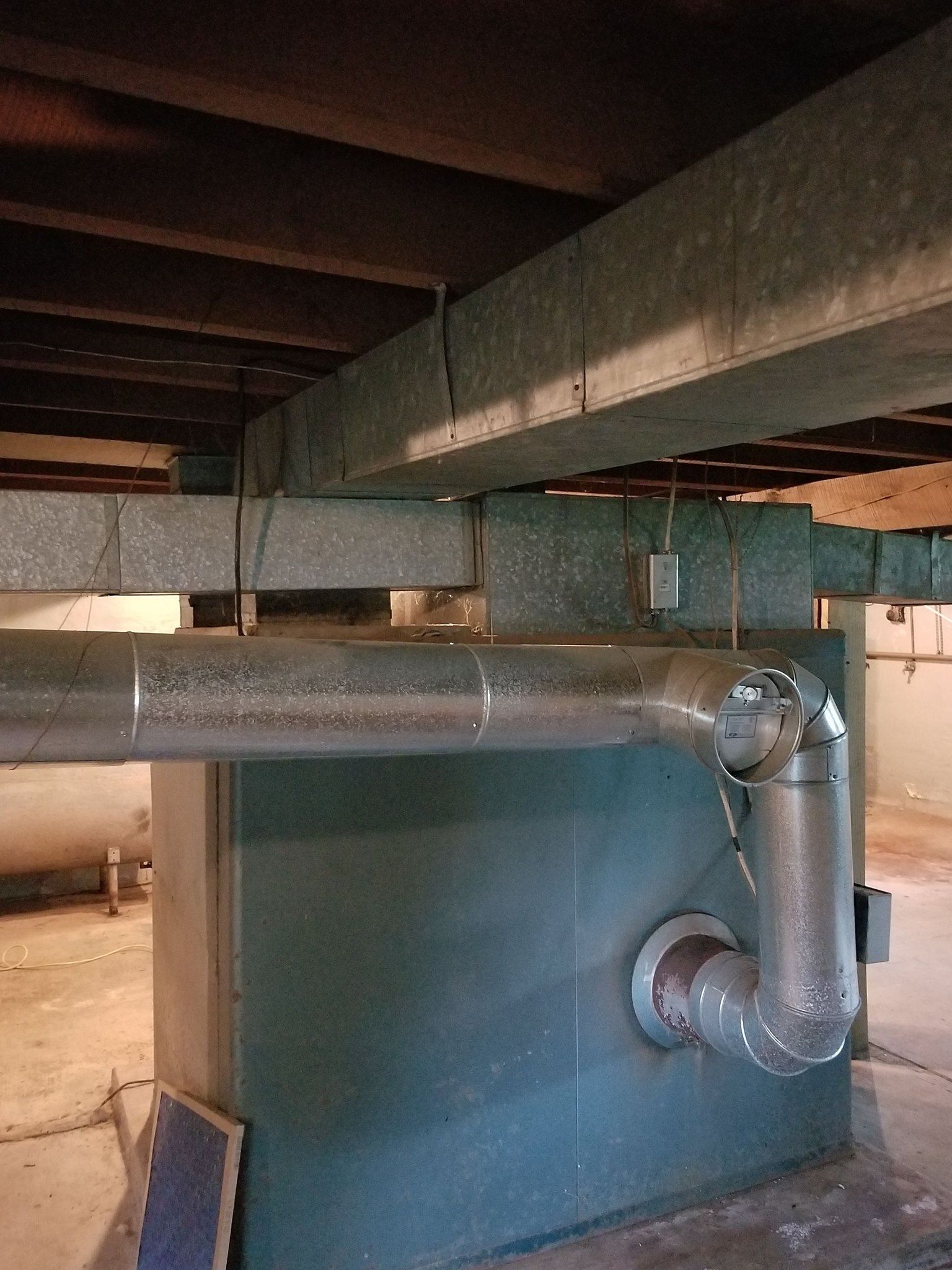 Furnace in a basement, silver ductwork, wooden beams overhead.