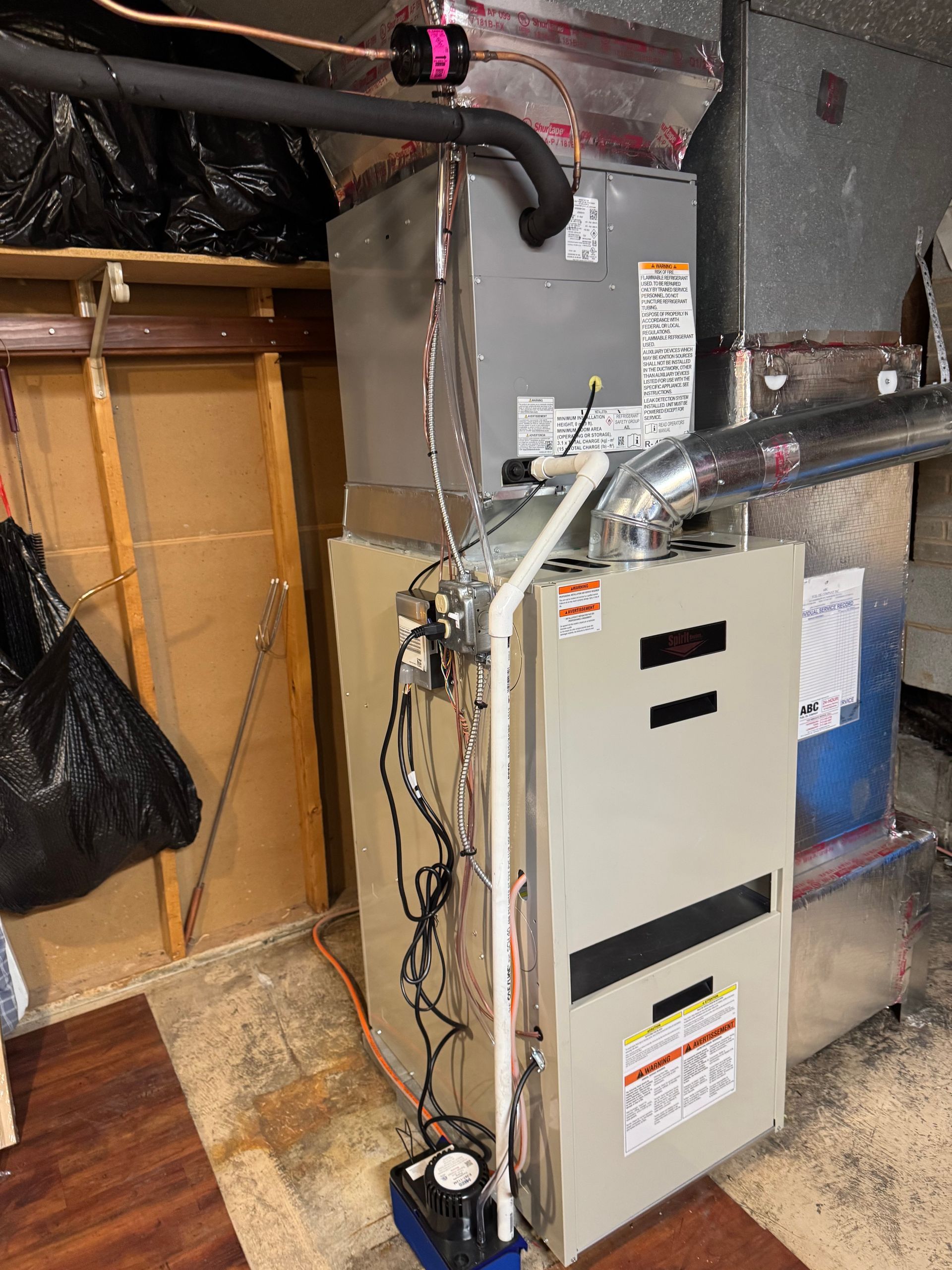 Furnace and air conditioning unit in a basement setting with ductwork and a condensate pump.