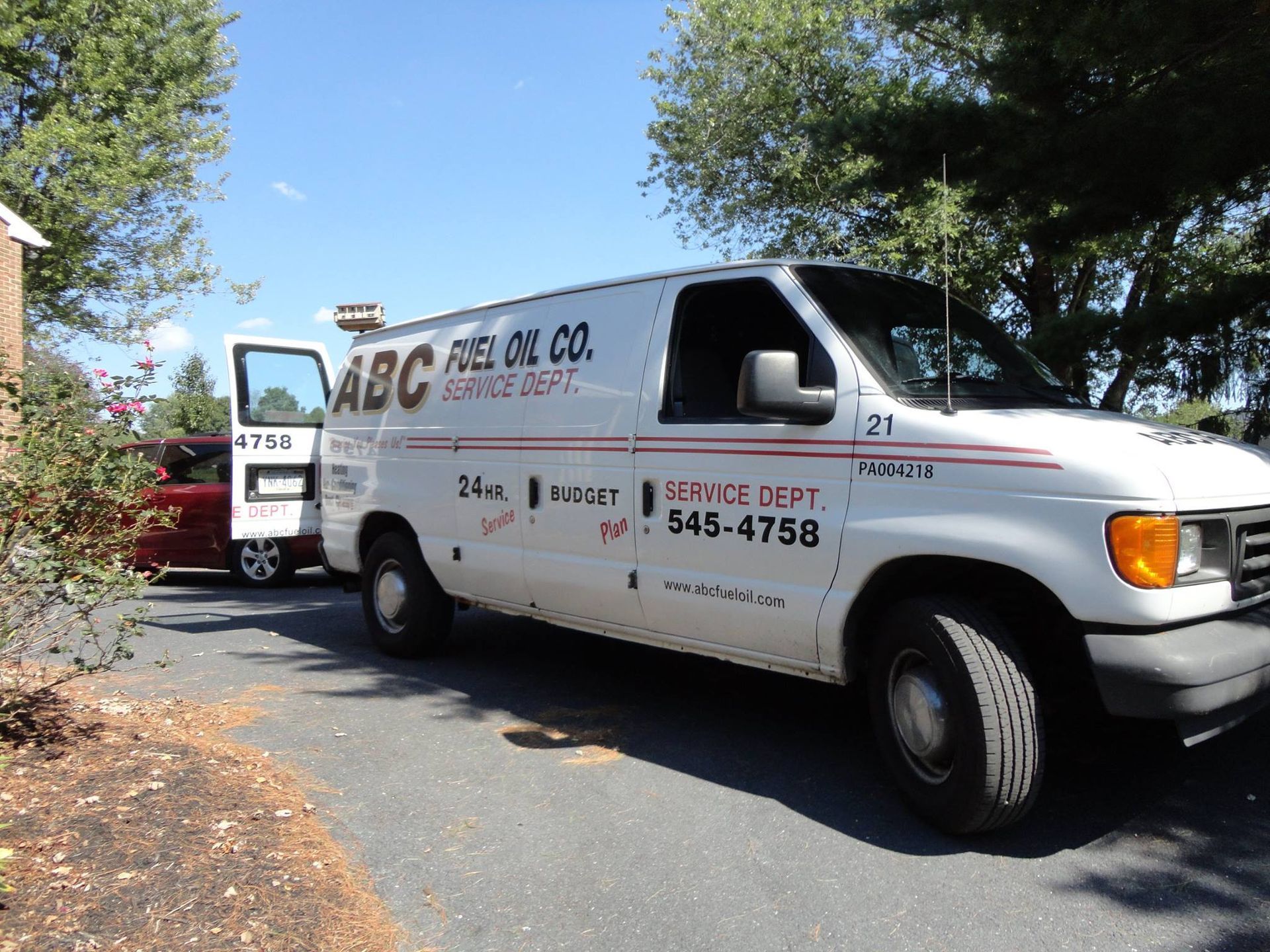 White ABC Fuel Oil Co. van parked in a driveway next to a red car. Door is open. Phone number visible.