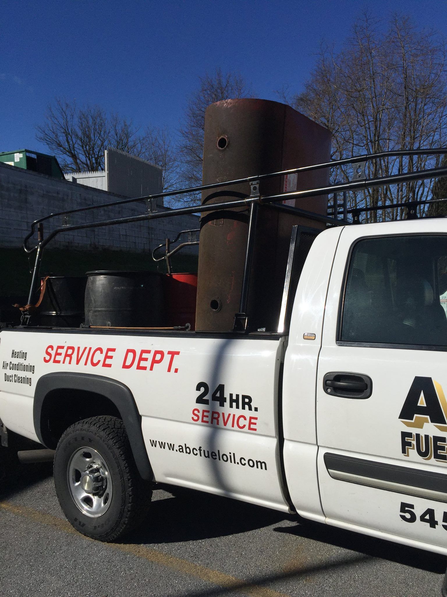 White pickup truck with fuel service logo carries large tanks on roof rack.
