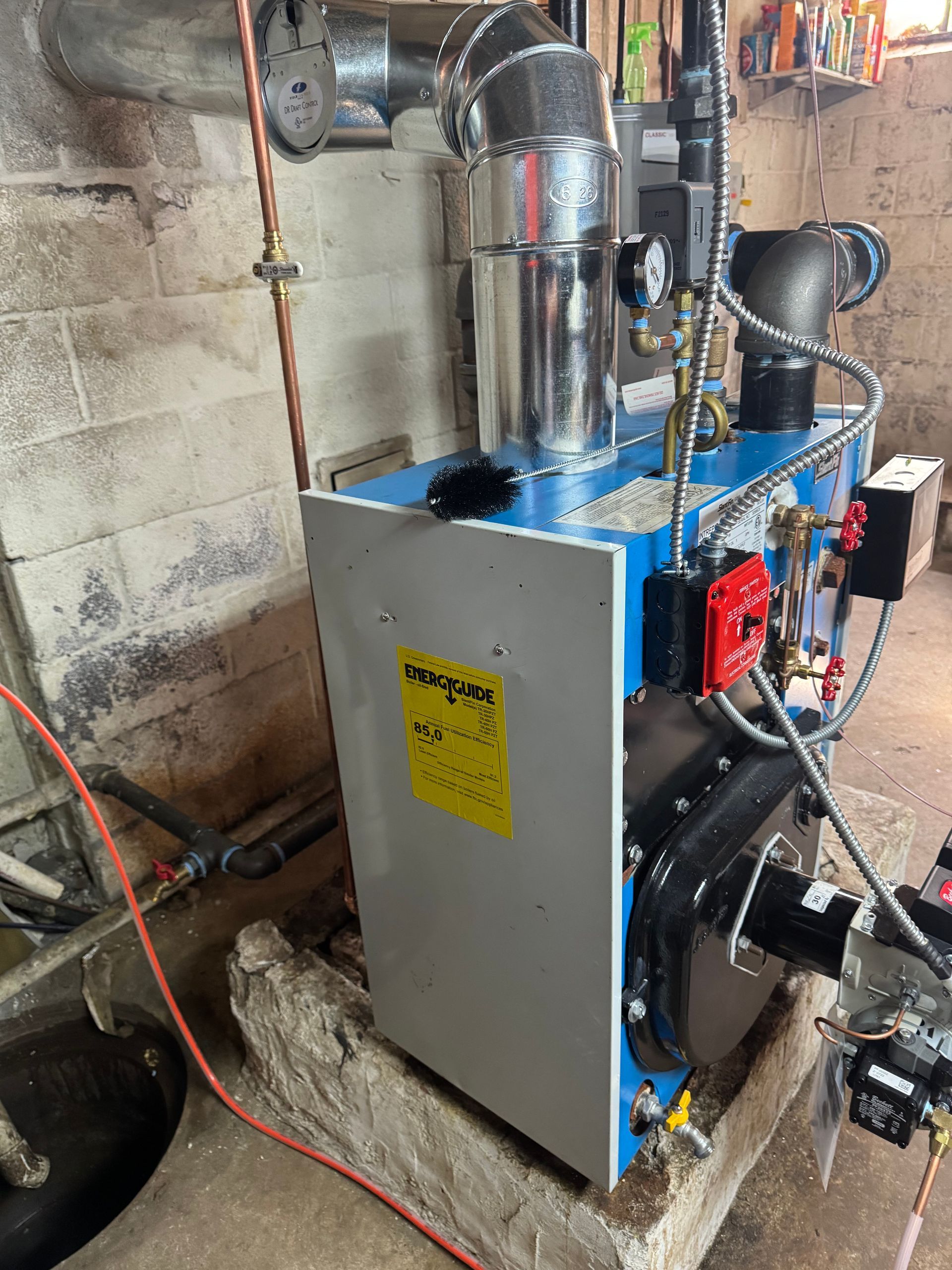 A blue and silver furnace in a basement setting with copper pipes. Yellow warning label on the front.