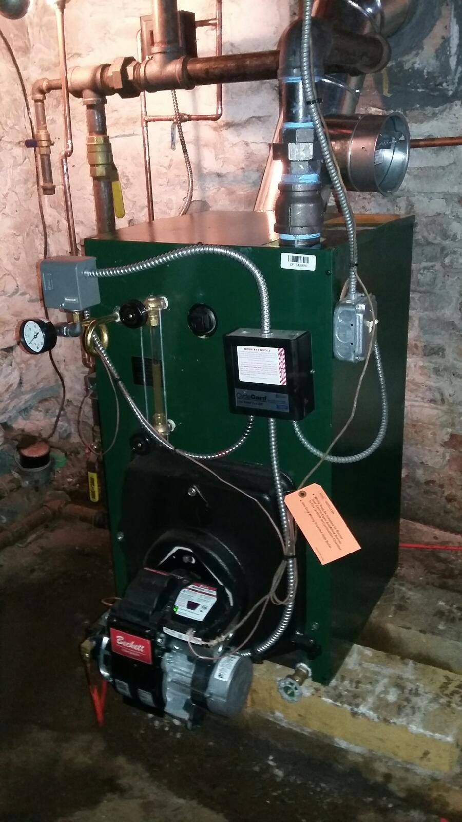Green oil-fired boiler in a basement. It has various pipes, gauges, and a burner.