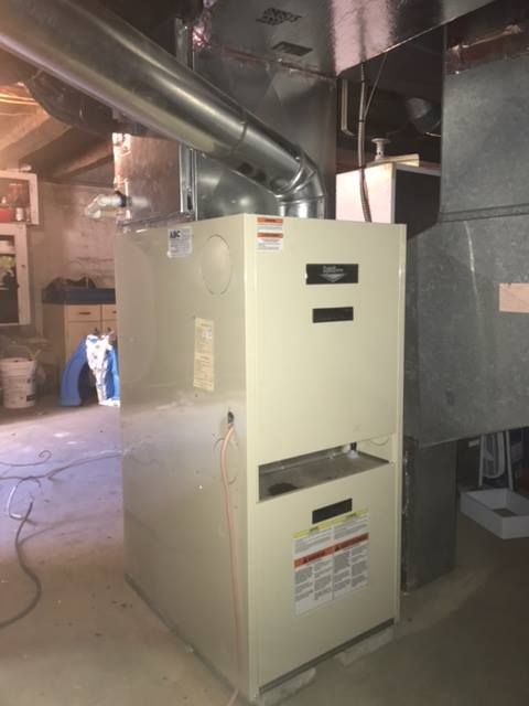 A tall, beige furnace with ductwork in a basement setting.