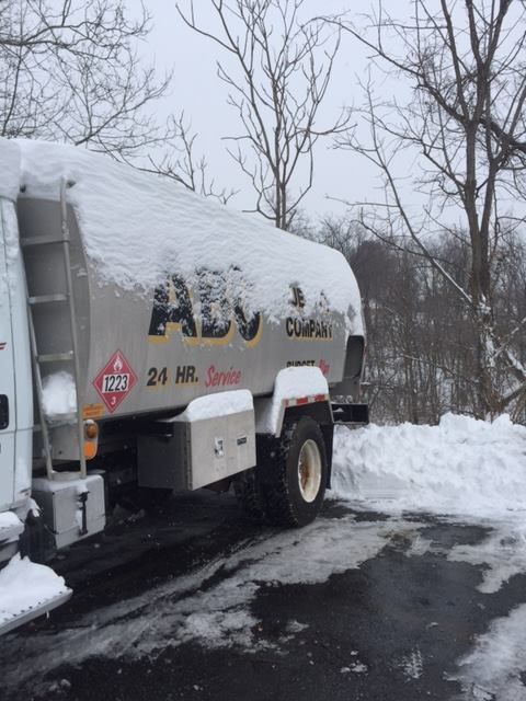 Tanker truck covered in snow parked in a snowy area, with bare trees in the background.