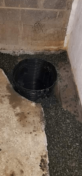 A black corrugated drainpipe in a basement corner, surrounded by gravel and concrete.