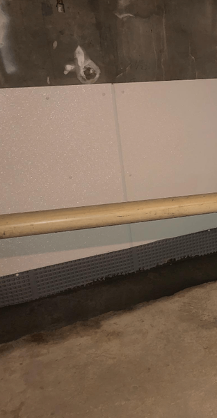 A light-colored pipe horizontally across a wall covered with white foam panels, set in a gray concrete room.
