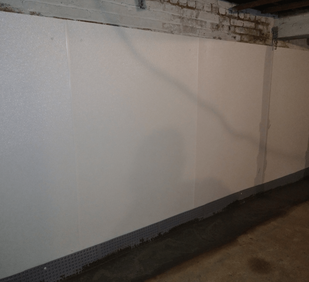 White-paneled basement wall with visible seams, set above a dark, textured base near a concrete floor.