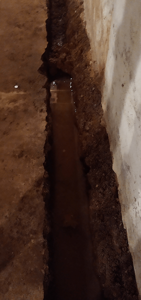 A narrow trench filled with water running alongside a concrete wall.