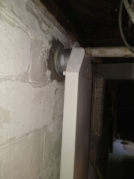 White vent pipe against a gray cinder block wall with some water stains.