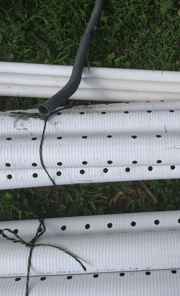 White perforated pipes with a black hose and twine on a grassy background.