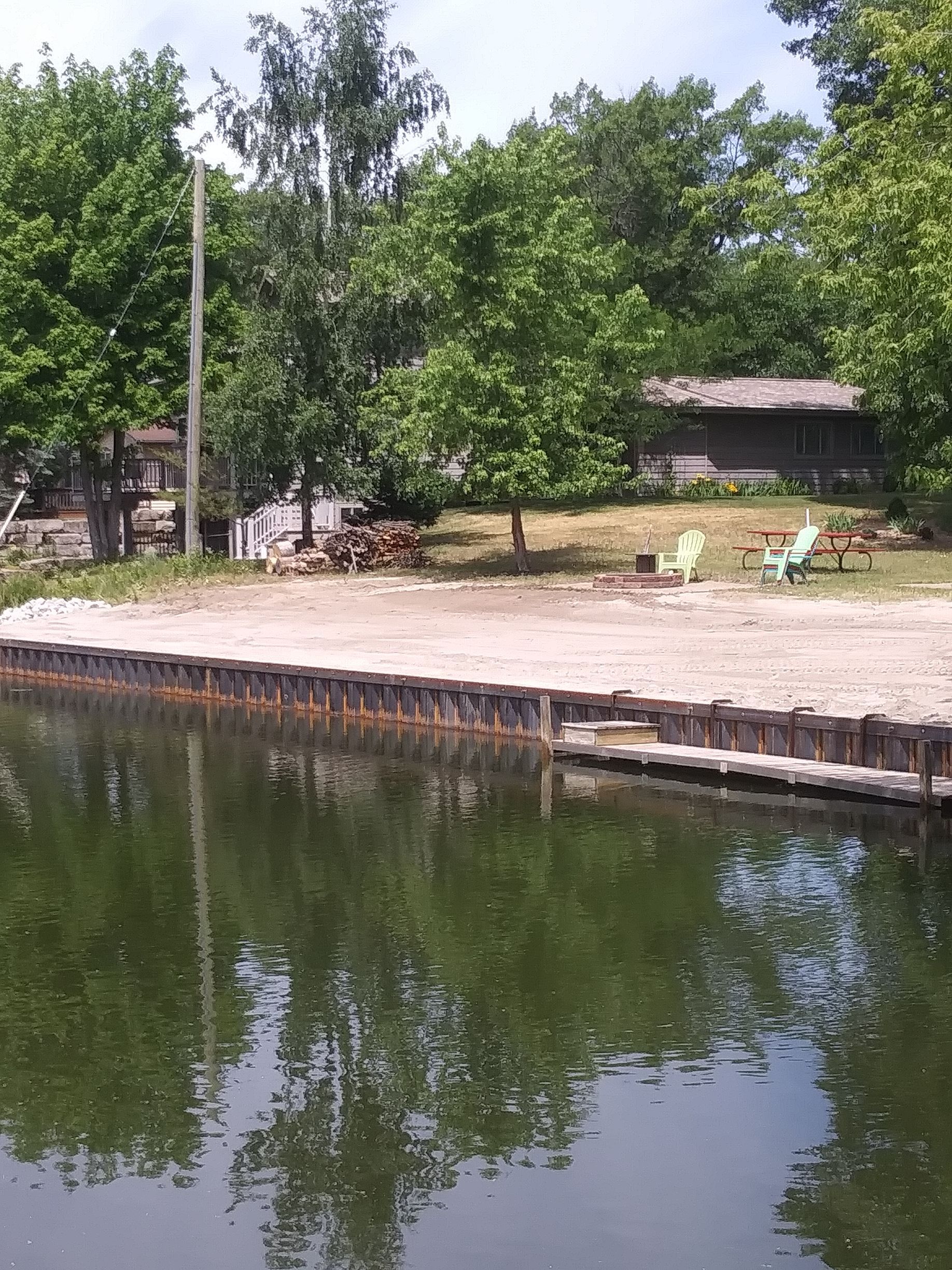 a dock with chairs on it is next to a body of water surrounded by trees 