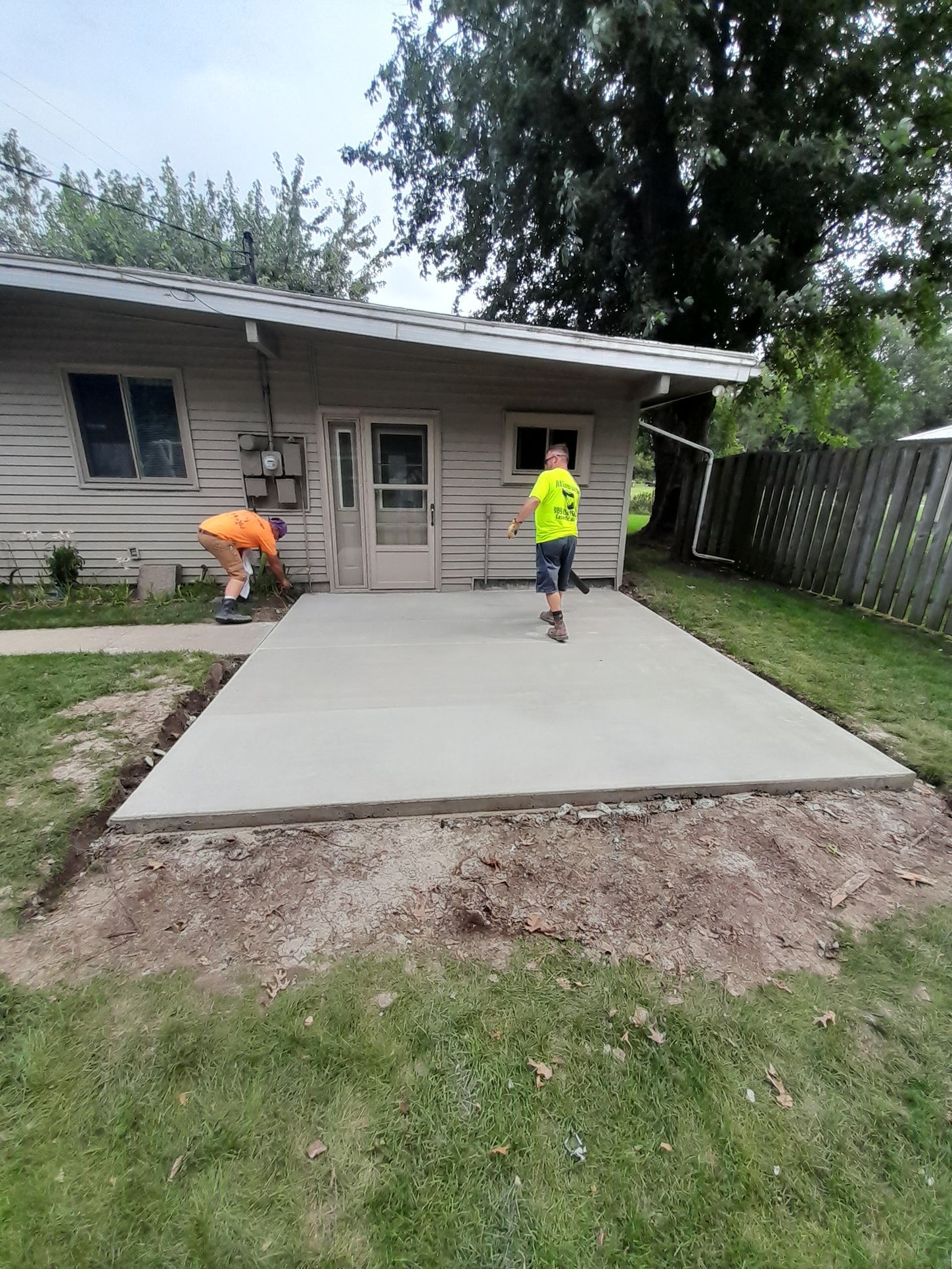 two men are working on a concrete patio in front of a house 