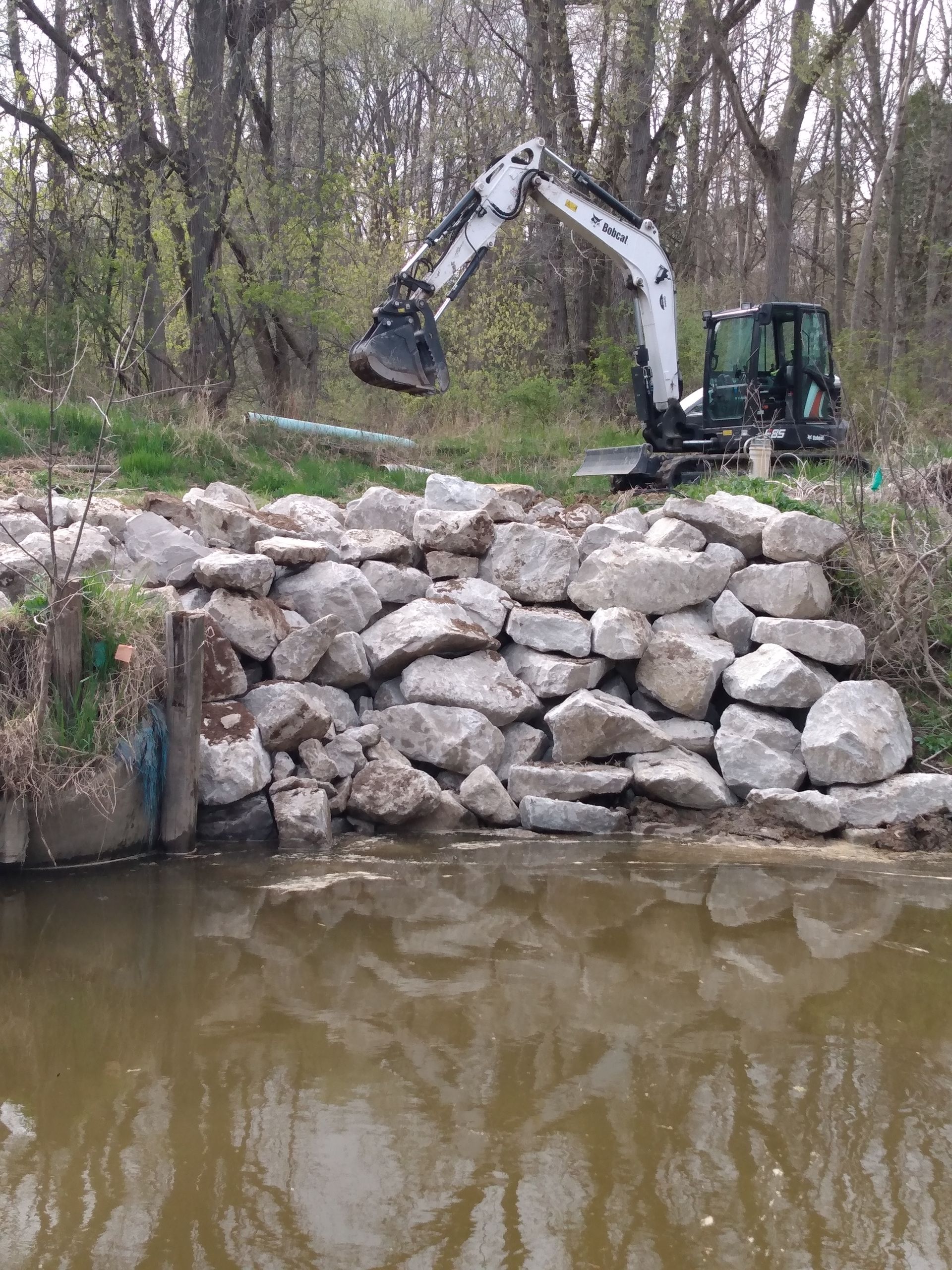 an excavator is working on a rock wall next to a river 