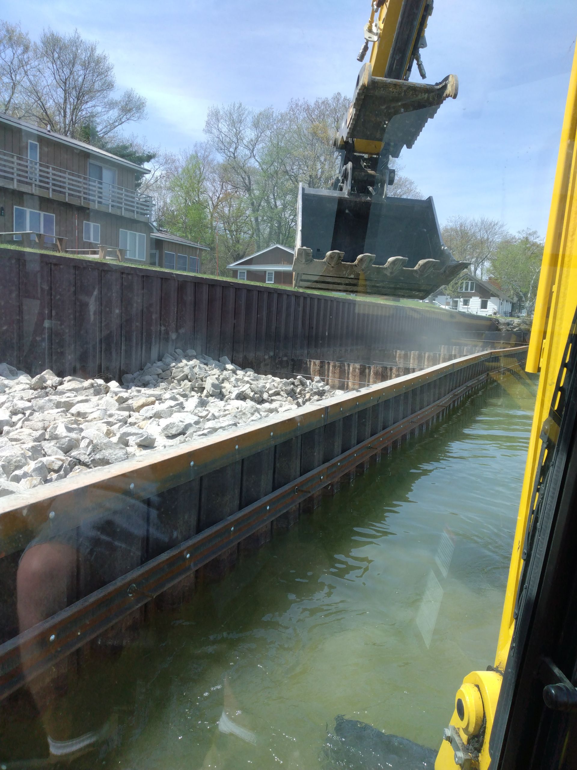 a yellow excavator is loading rocks into a body of water 