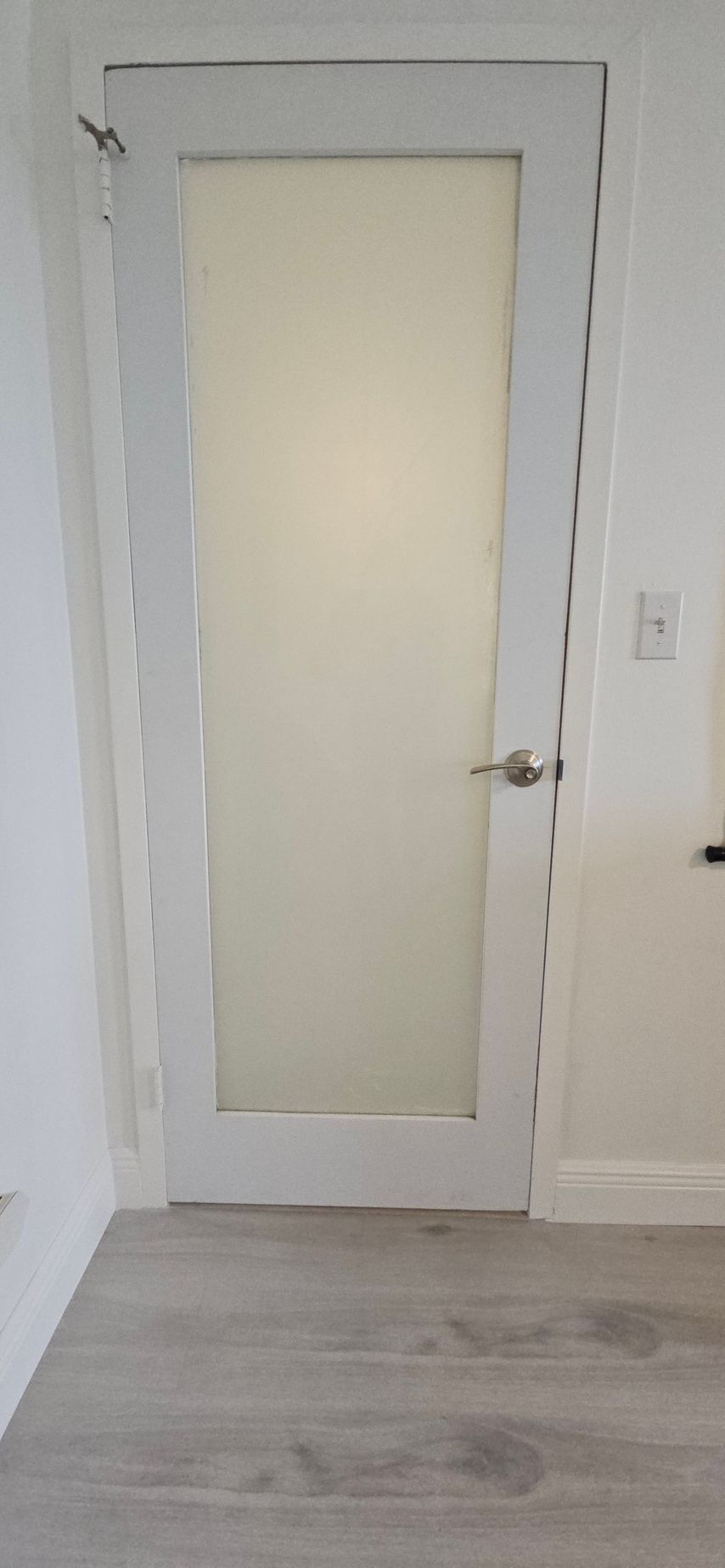 White door with frosted glass panel in a white framed doorway with a metal handle, situated in a room with light grey flooring.