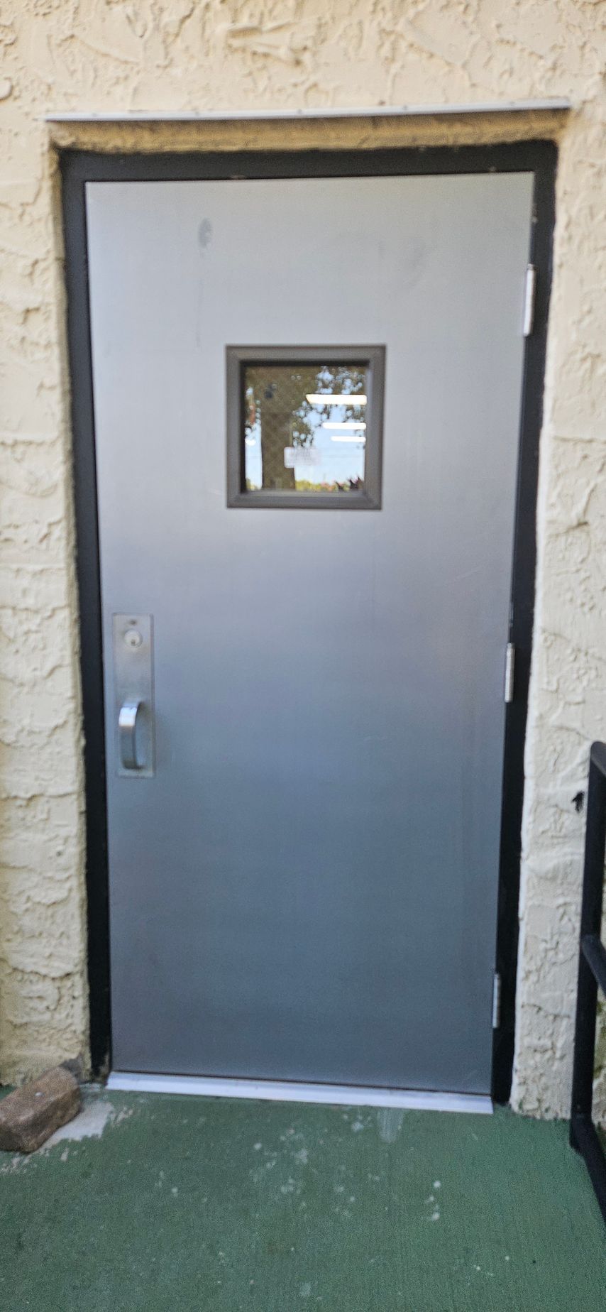 Metal door with a small window, set in a light-colored stucco wall.