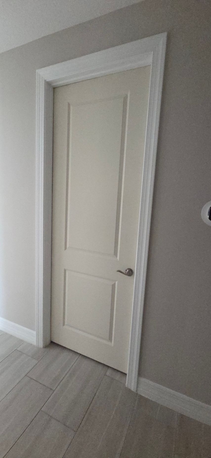 A white door with two panels and silver handle in a room with light grey walls and tile flooring.